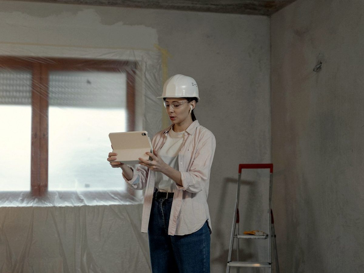 Femme en casque de chantier consultant une tablette dans une pièce en travaux