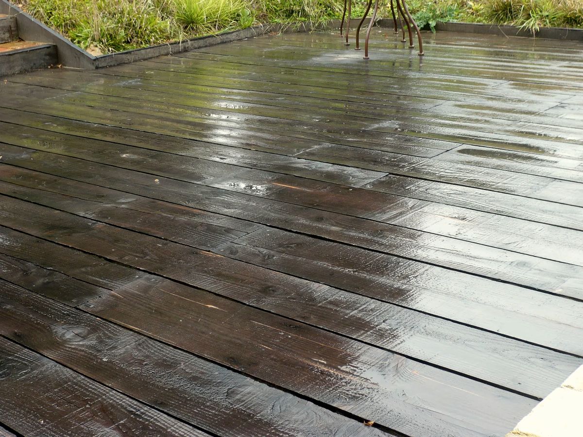 Terrasse en lames de bois mouillées après une averse, au pied d'une maison