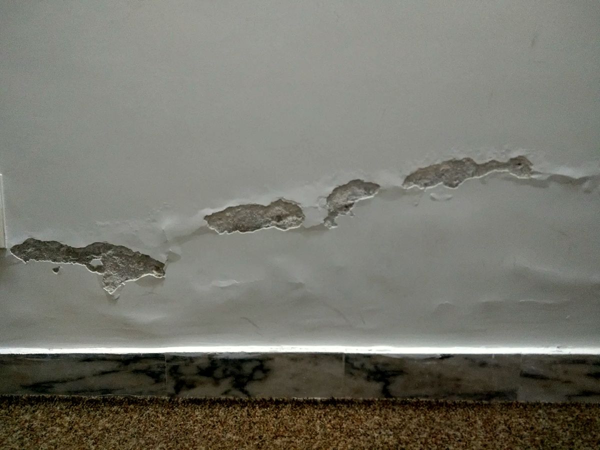 Bas de mur intérieur marqué par l'humidité qui remonte du sol, peinture cloquée
