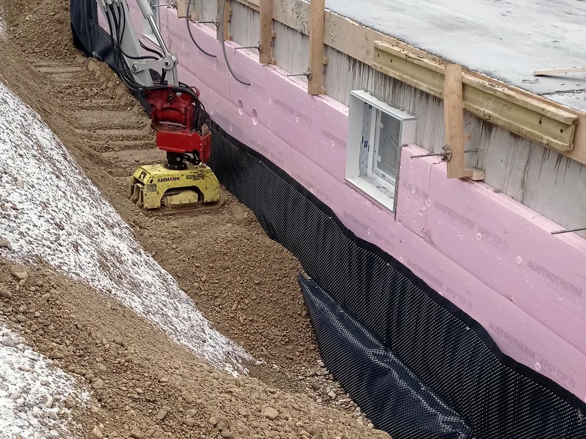 Étanchéité verticale noire appliquée sur un mur enterré, fouille ouverte le long de la maison